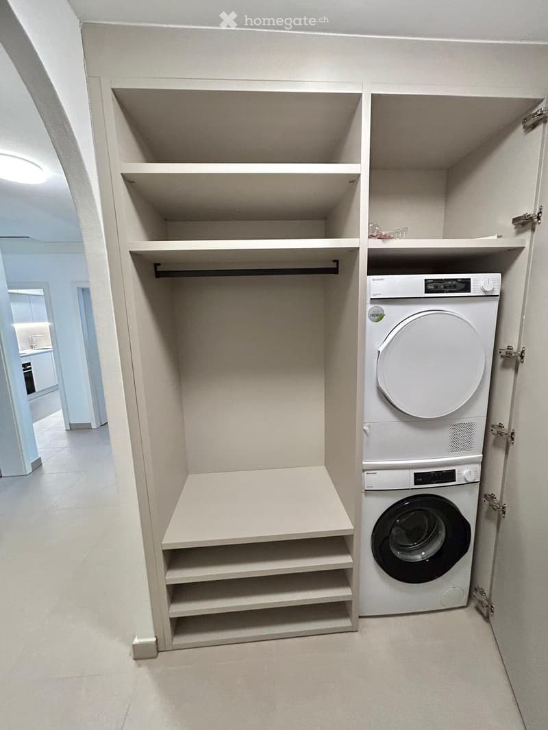 A well-lit laundry room with built-in shelves and a stacked washer-dryer unit.