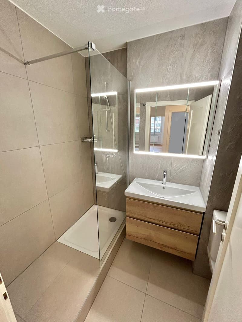 Modern bathroom with a glass-enclosed shower, a wooden vanity with a sink, and a large mirror with LED lighting.