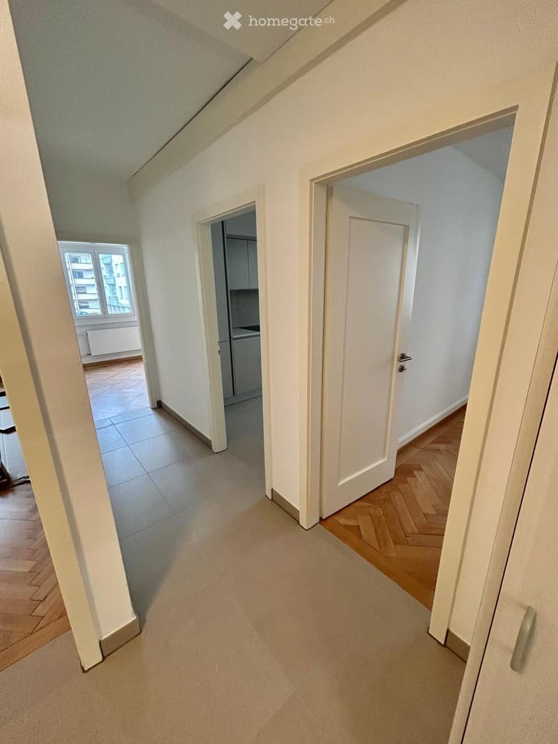 Empty hallway with white walls, wooden flooring, and multiple doors leading to different rooms.