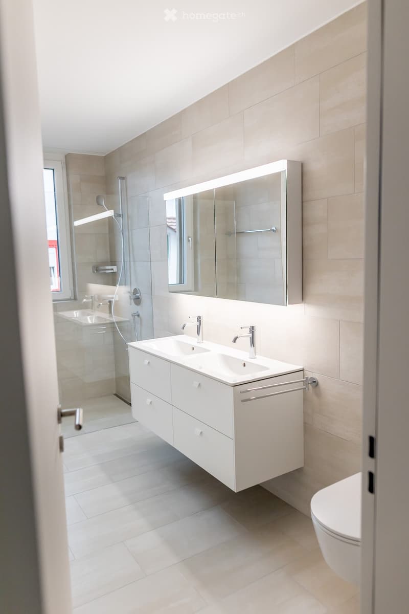 Modern bathroom with a double sink vanity, large mirror, toilet, and glass-enclosed shower area.