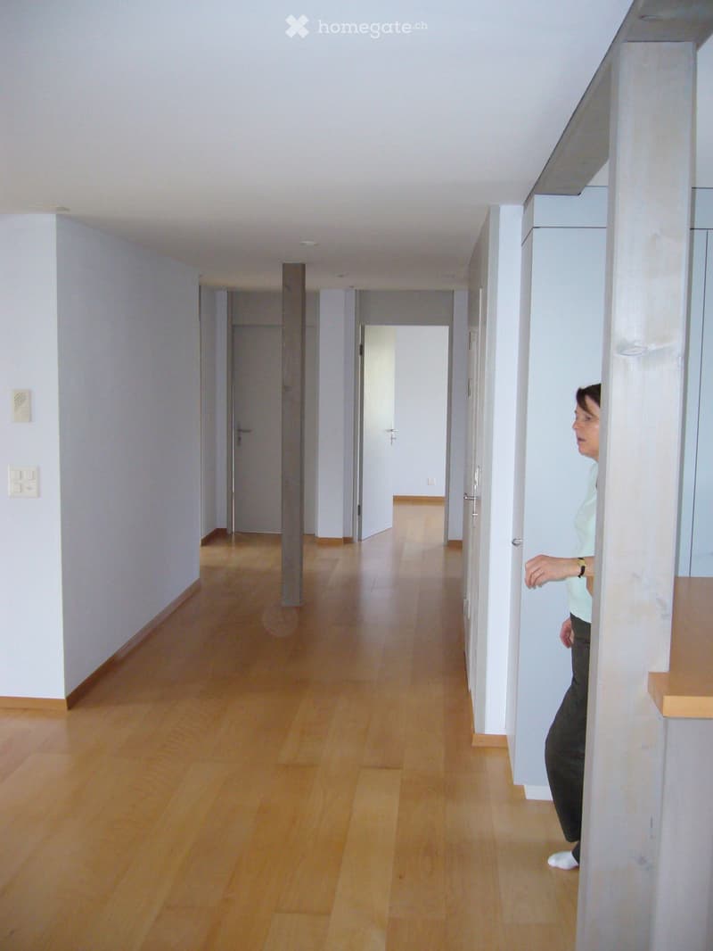 Empty hallway with wooden flooring, white walls, and multiple doors leading to rooms.