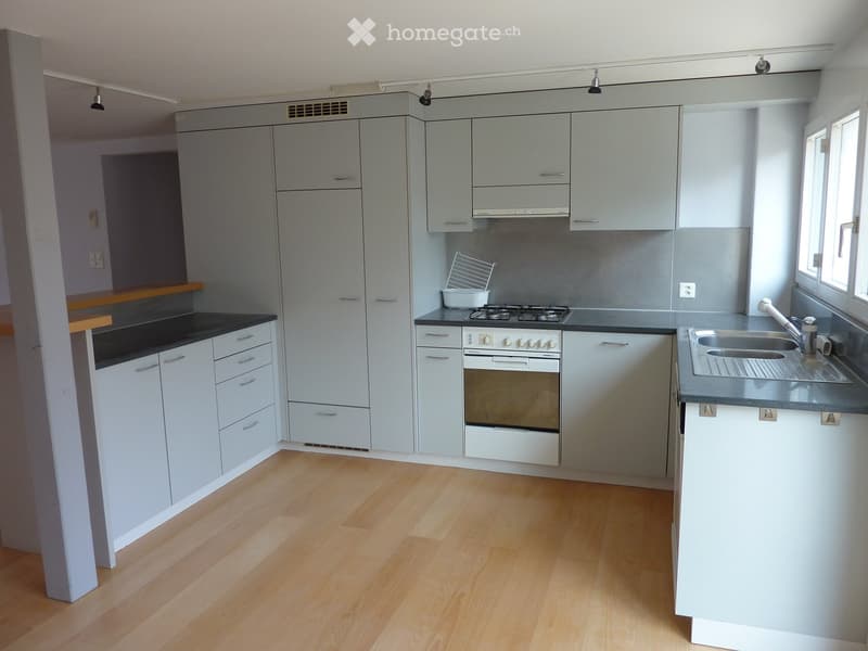 Modern kitchen with light grey cabinets, black countertops, a gas stove, and a stainless steel sink.
