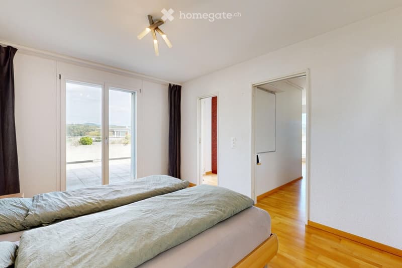 Bright bedroom with two single beds, wooden flooring, large sliding glass doors leading to a balcony, and modern lighting fixture.