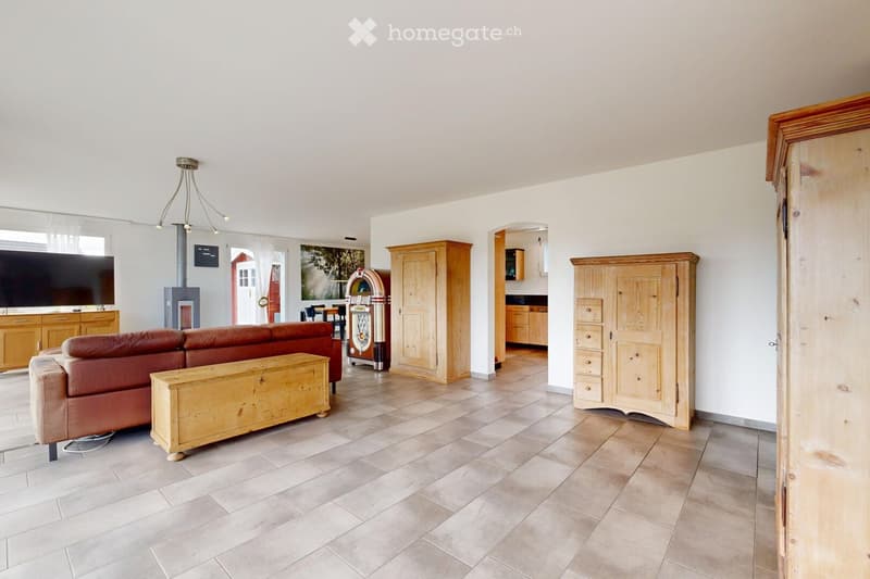 A spacious living room with a red leather sofa, wooden coffee table, chandelier, and a jukebox. The room features a fireplace, large windows, and wooden cabinets.