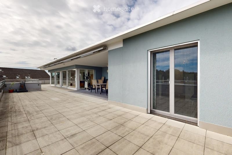 Spacious balcony with tiled flooring, large sliding glass doors leading to an indoor dining area, modern light fixtures, and a view of neighboring rooftops.