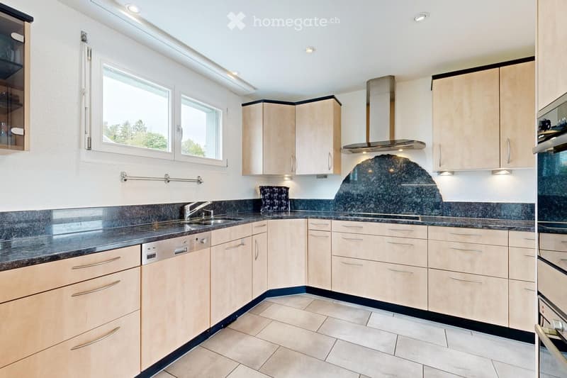 Modern kitchen with light wood cabinets, granite countertops, stainless steel appliances, and a central island.