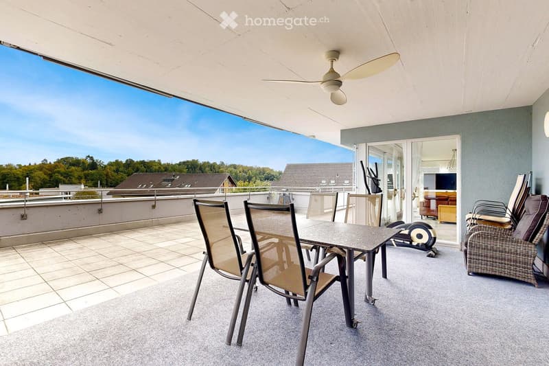 Balcony with a dining table, chairs, and a ceiling fan, overlooking a scenic view of trees and rooftops.