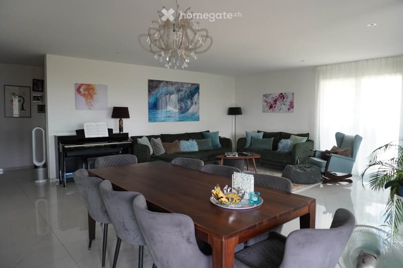 A modern living room with a large wooden dining table, multiple chairs, a sofa, a piano, and decorative items including lamps and artwork.