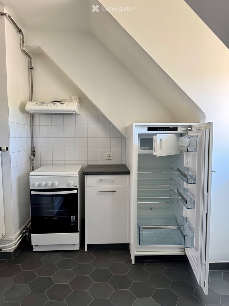 Compact kitchen with white oven, open refrigerator, and white cabinets under a slanted ceiling.