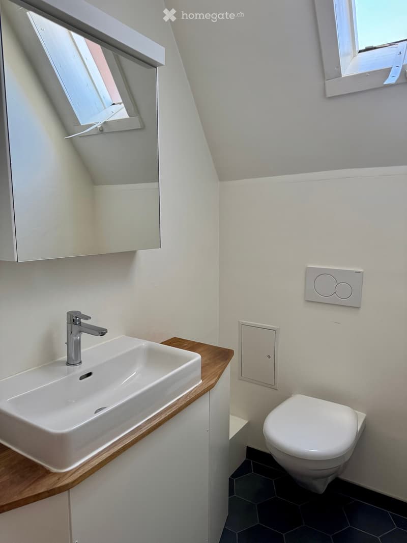 Modern bathroom with a white sink, chrome faucet, and a toilet. Features a wooden countertop and white walls.