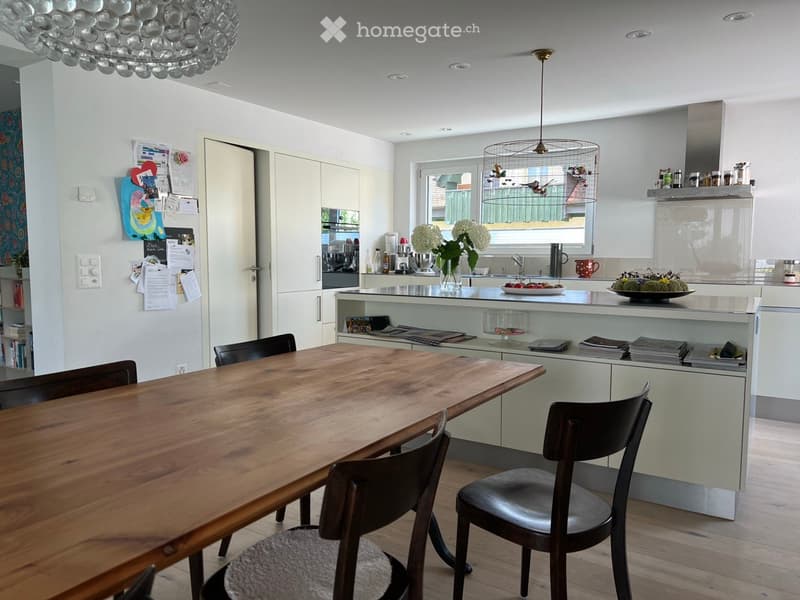Modern kitchen and dining area with a wooden dining table, chairs, kitchen island, refrigerator, and various appliances.
