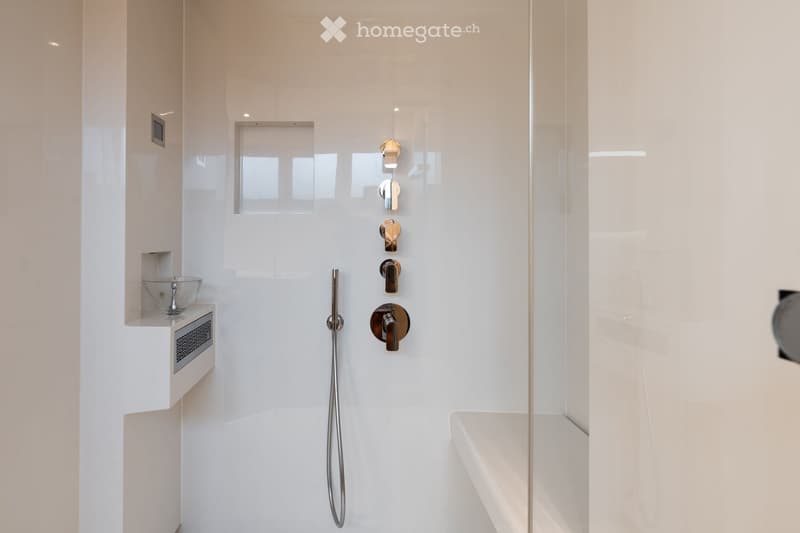 Modern bathroom with white tiles, a glass shelf holding a bowl, and a sleek shower area with multiple faucet options.