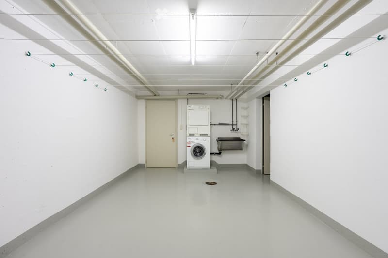 A clean, unfurnished room with a washing machine, a door, and a sink.