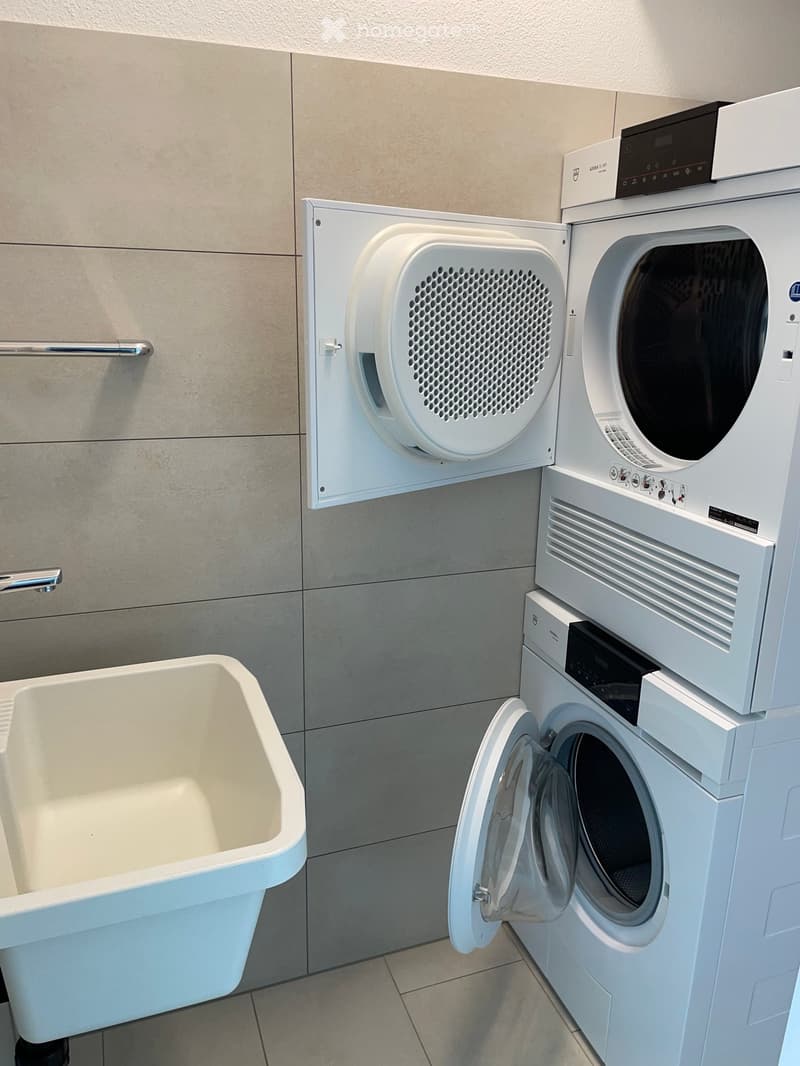 Bathroom with a white bathtub, a washing machine, and a dryer unit.