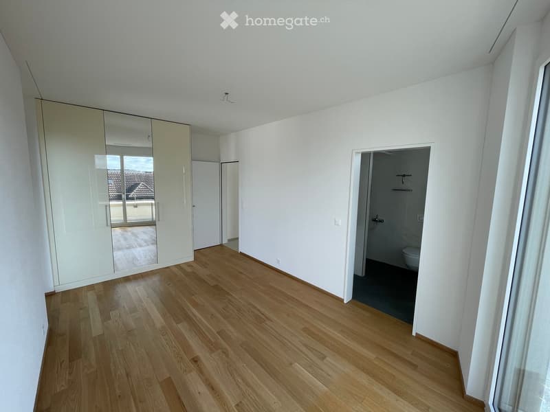 Empty room with light wooden flooring, white walls, and a large mirrored wardrobe. A doorway leads to a small bathroom with a toilet visible.