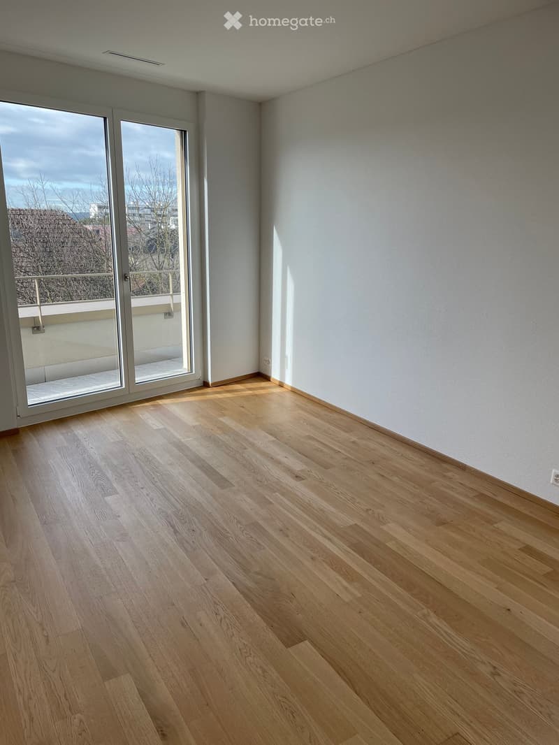 Empty room with light wooden flooring, white walls, and large sliding glass doors leading to a balcony.