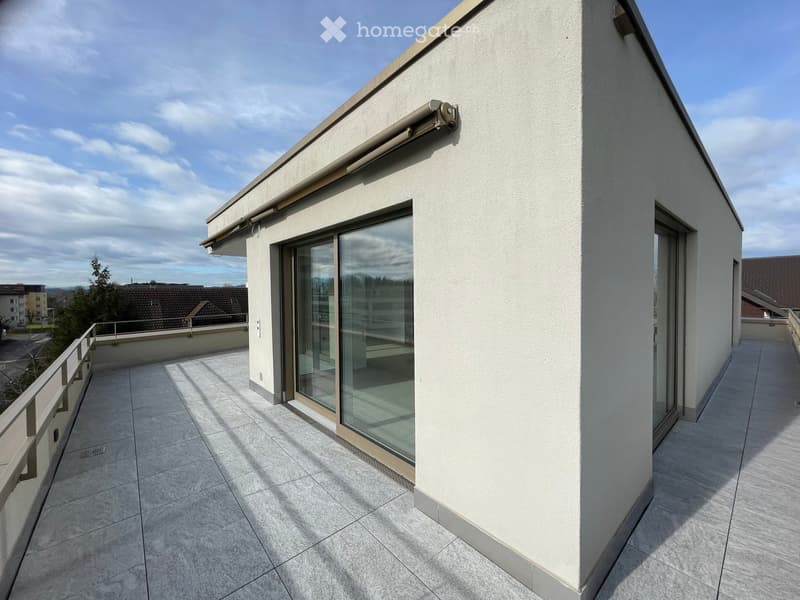Modern balcony with tiled flooring, white walls, large glass sliding doors, and a metal railing.