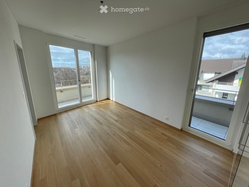 Empty room with light wooden flooring, white walls, and large glass sliding doors leading to a balcony.