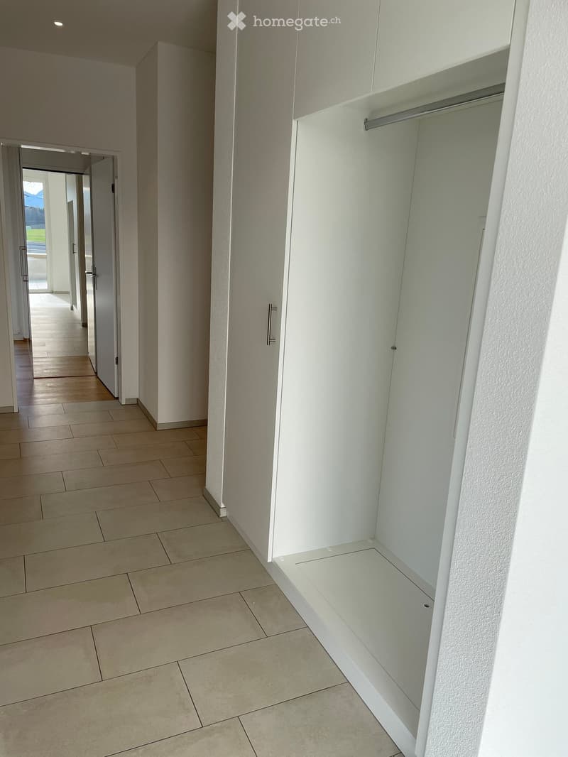 Empty hallway with tiled floor, white walls, and built-in closet with empty shelves and hanging rod.