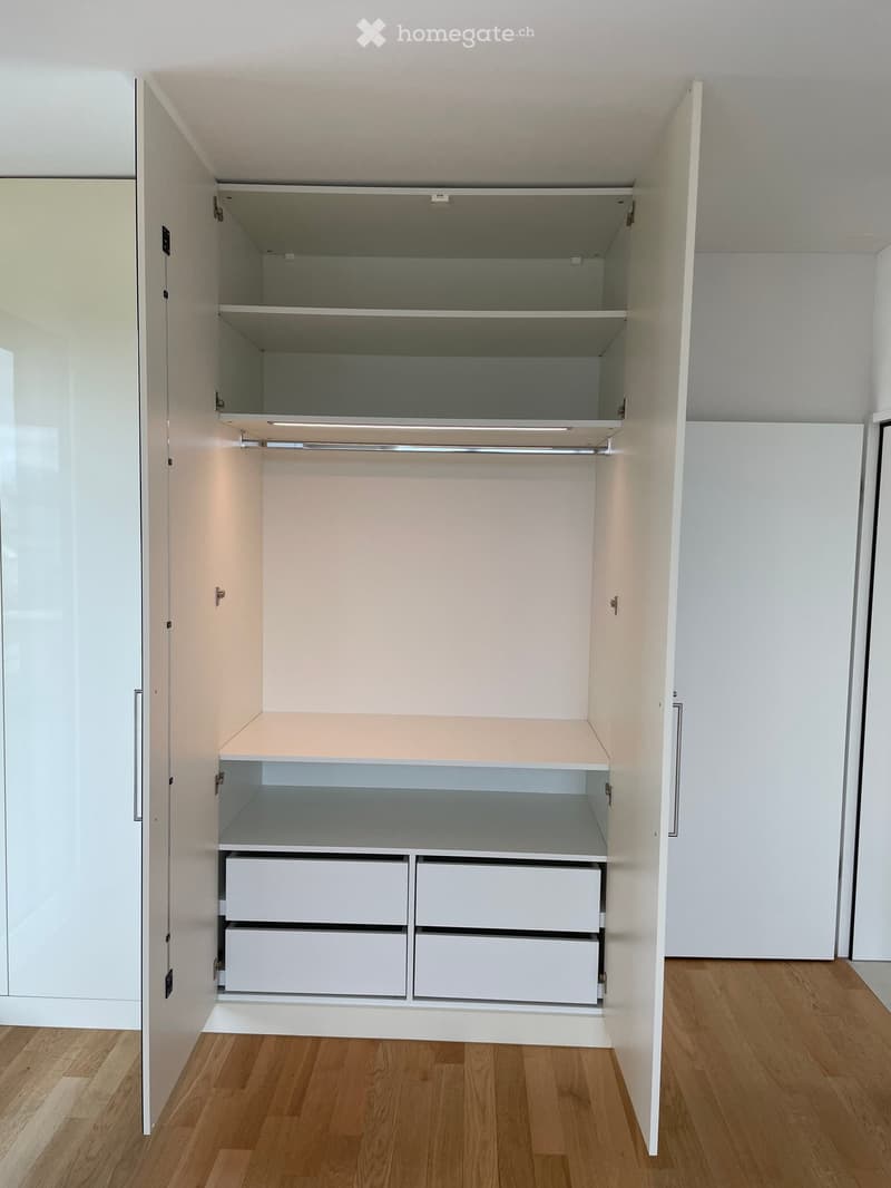 Empty room with wooden flooring and built-in white closet with shelves and drawers.