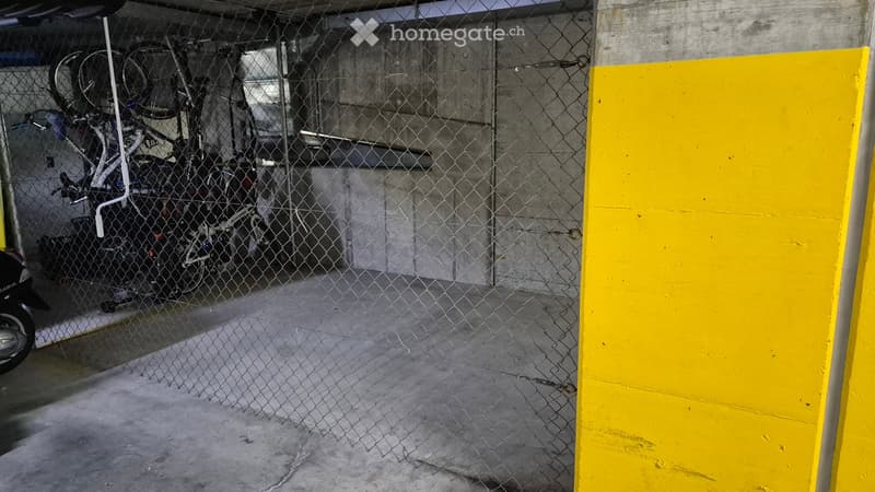 Bicycles parked behind chain link fence, yellow painted concrete wall.