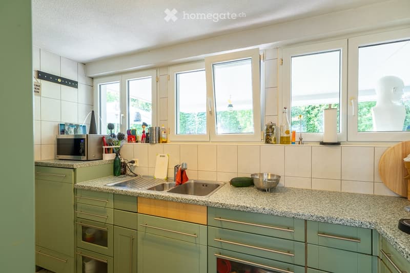 A modern kitchen with green cabinets, granite countertops, and stainless steel appliances. The kitchen features a double sink, microwave, and various kitchen items on the countertops.