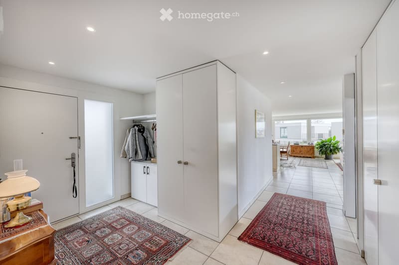 Bright hallway with white walls, tiled floor, built-in wardrobes, and decorative rugs leading to adjacent rooms.