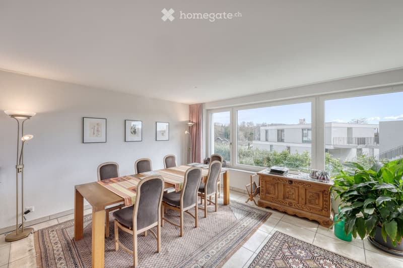 Bright dining room with large windows, wooden dining table, six chairs, floor lamp, decorative cabinet, and potted plant.