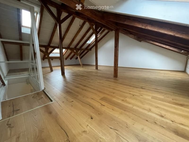 Empty attic space with wooden beams and exposed wooden floor, featuring skylights and a glass door leading to a balcony.