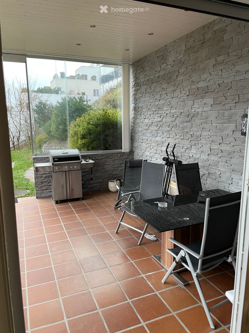 Balcony with tiled floor, stone wall, grill, table, and chairs.