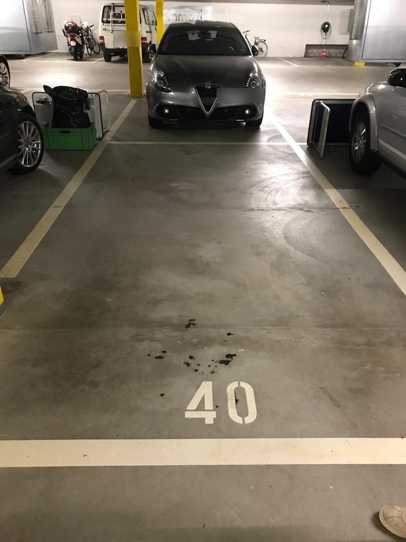 Underground parking lot with several parked vehicles including a car, motorcycle, bicycle, and van. The floor is marked with parking spaces and the number "40" is prominently displayed.
