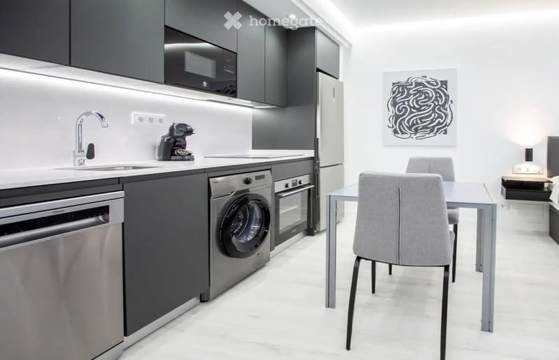 Modern kitchen and dining area with stainless steel appliances, white countertops, and grey cabinets. Includes a sink, coffee maker, dishwasher, washing machine, oven, refrigerator, dining table, and chairs.