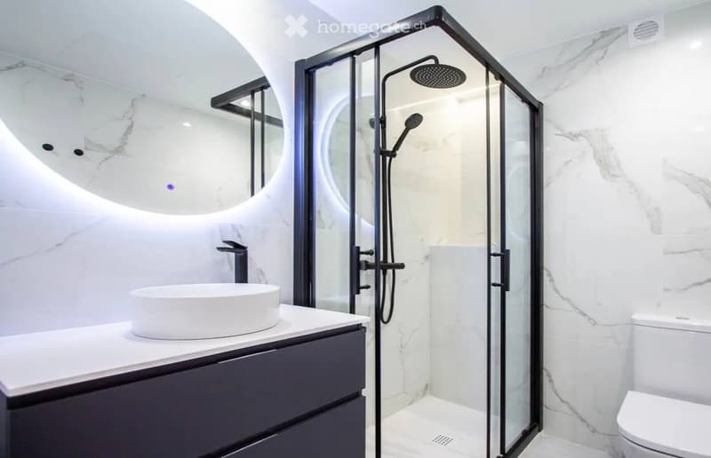 Modern bathroom with marble walls, a sleek sink, a glass-enclosed shower, and a toilet.
