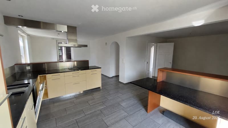 Modern kitchen with light-colored cabinets, black countertops, and stainless steel appliances including a stove and range hood. The space features an open layout with a central island and ample storage.