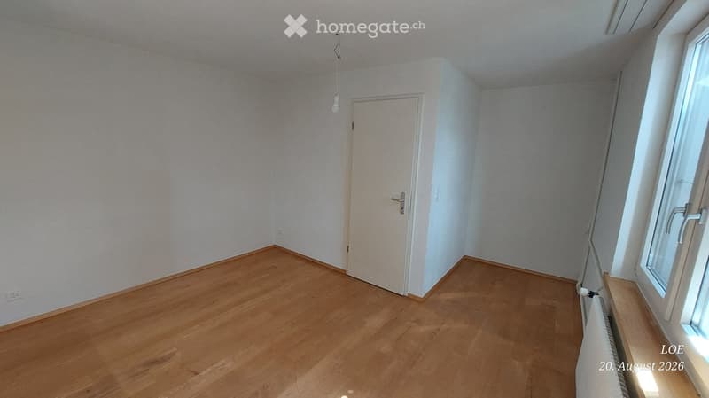 Empty room with wooden flooring, white walls, a single door, and a window with a radiator below it.