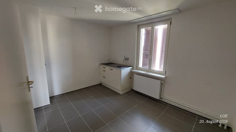 Empty room with tiled floor, white cabinet, sink, window with blinds, radiator, and door.