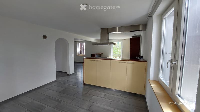 Modern kitchen with light-colored cabinets, a countertop, and a stainless steel range hood. The space features tiled flooring and large windows allowing natural light.
