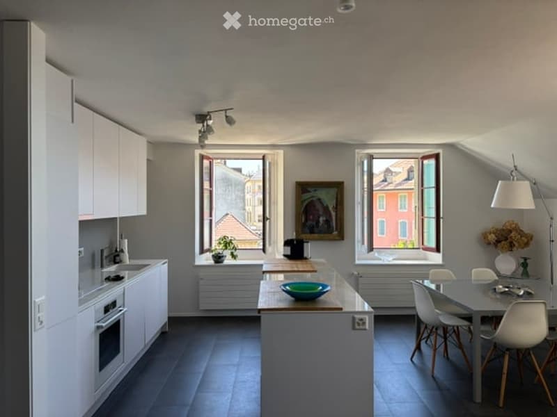 Modern kitchen with white cabinets, central island, dining area, and large windows offering a city view.