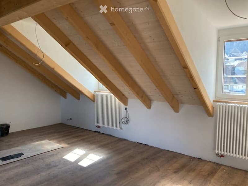 empty attic room with wooden beams, wooden floor, white walls, two radiators, window