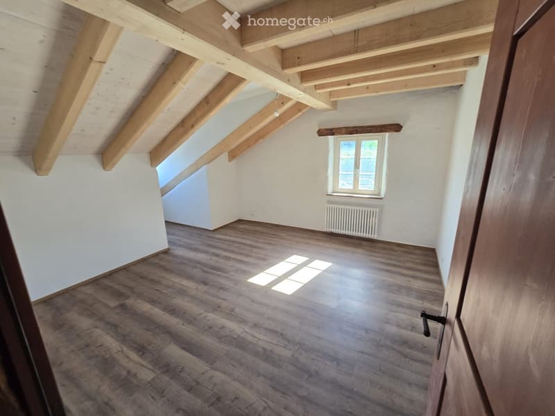 Empty attic room with wooden beams, wooden flooring, and a window letting in natural light.