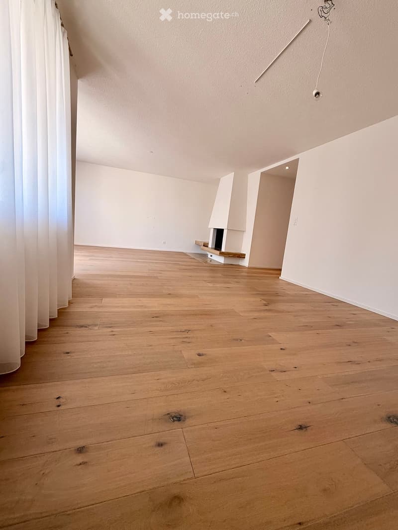 Empty room with wooden flooring, white walls, and a small built-in fireplace in the corner.
