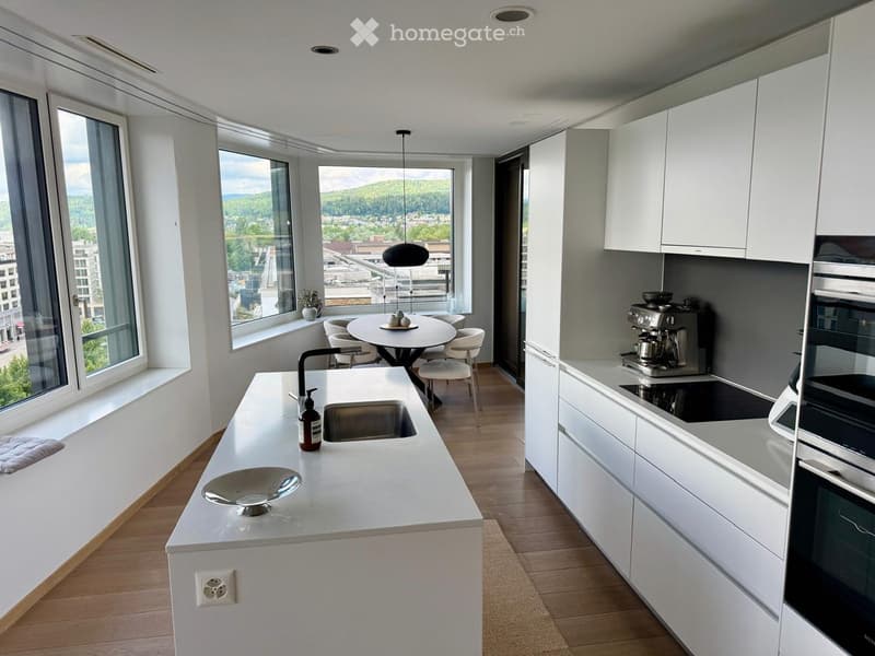 Modern kitchen with white cabinets, a central island, and a dining area. Features include a sink, coffee maker, oven, and a round dining table with chairs.