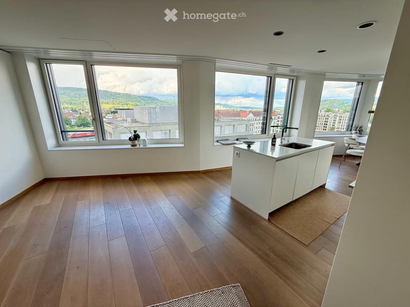 Modern kitchen with white cabinets, wooden flooring, large windows offering a scenic view, and a small seating area with a table and chairs.