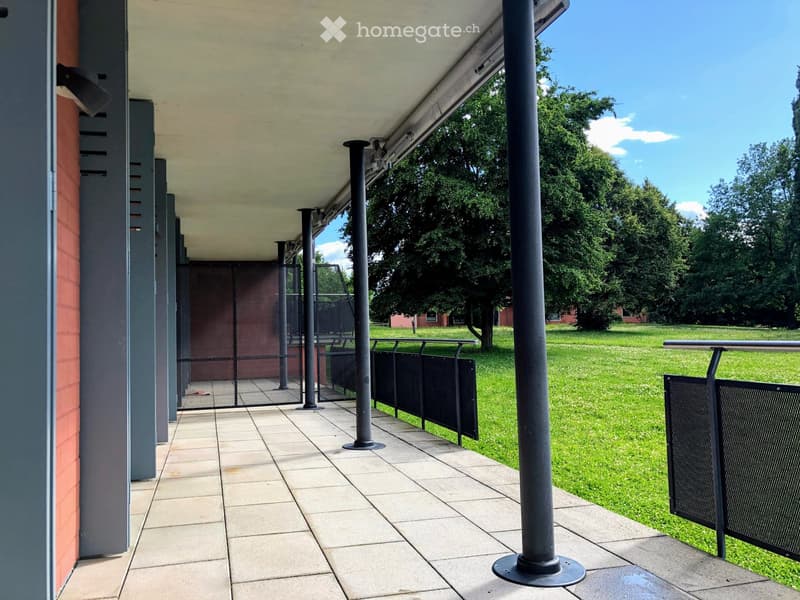 Covered outdoor area with tiled floor, metal railings, and black posts, leading to a grassy lawn.