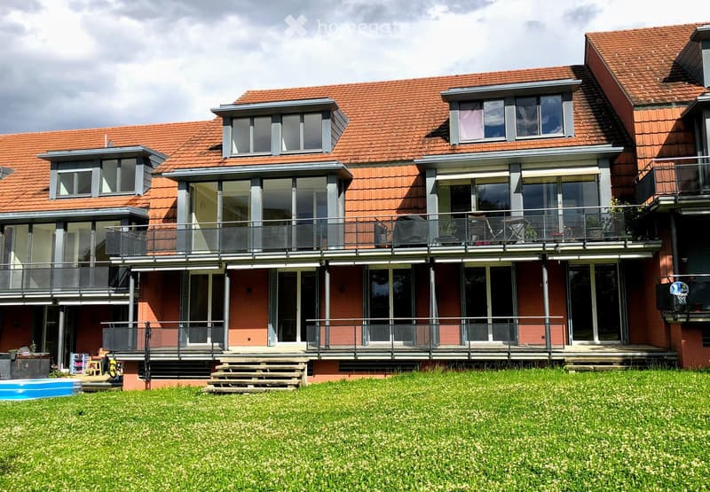 Modern two-story house with red-tiled roof, large windows, multiple balconies, and a swimming pool in the front yard.