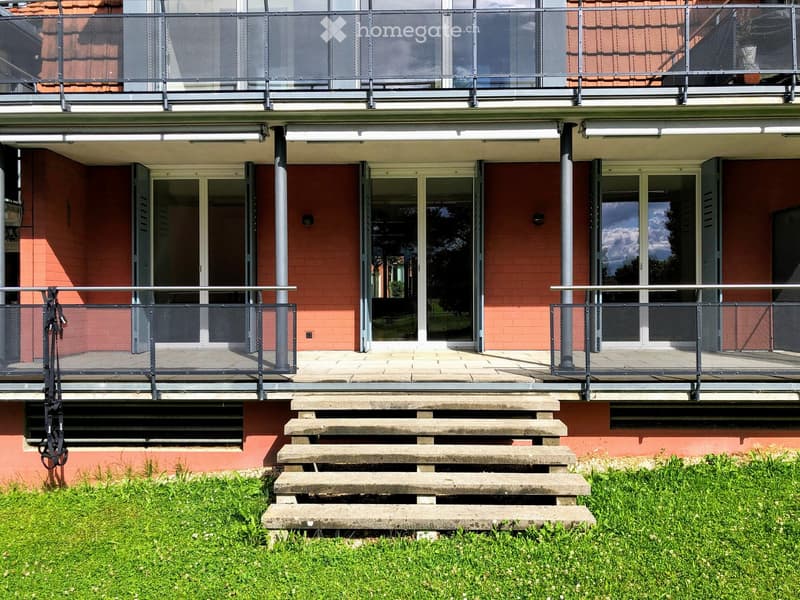 Balcony with metal railings, steps leading up, and a view of the building facade with large windows and a covered entrance area.