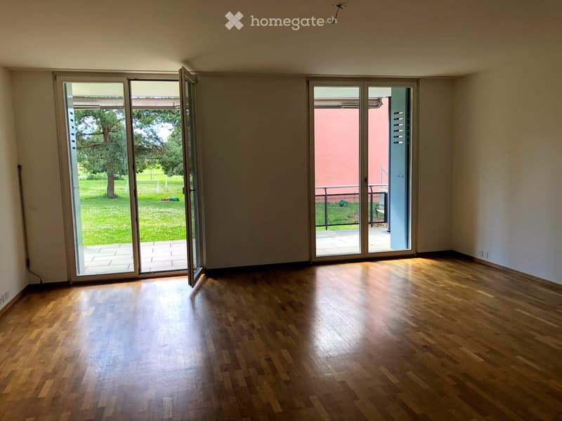 Empty room with wooden flooring and large sliding glass doors leading to a balcony and garden area.