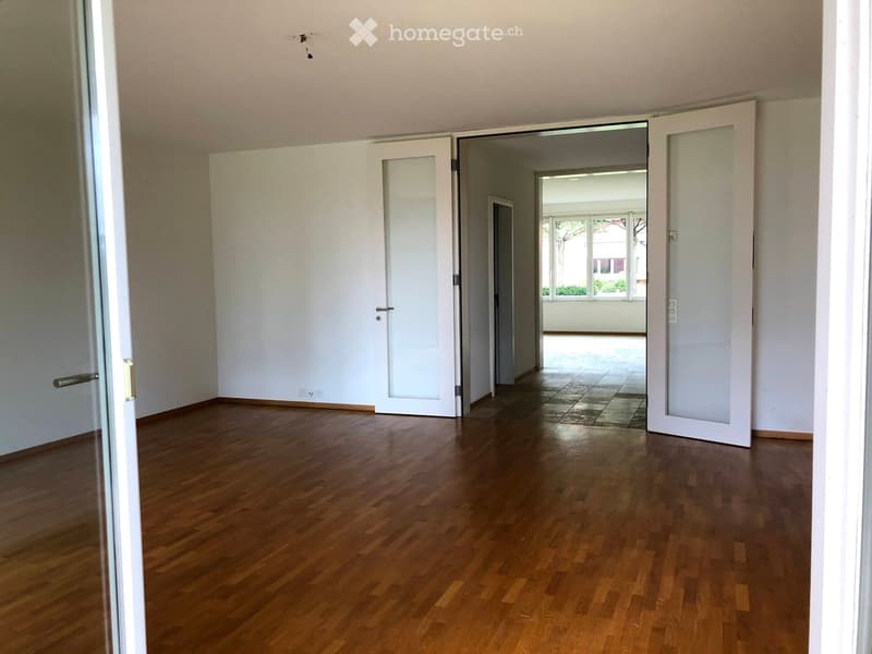 Empty room with wooden flooring, white walls, and multiple doors leading to other spaces.