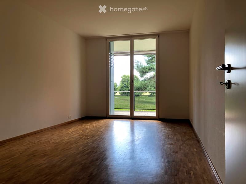 Empty room with wooden flooring, large sliding glass doors leading to a balcony, and natural light streaming in.