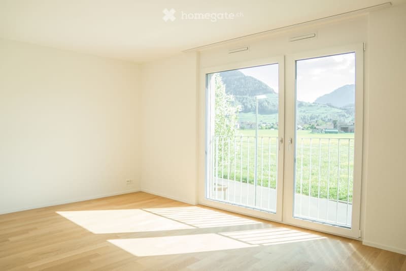 Empty room with wooden flooring, large sliding glass doors leading to a balcony with a scenic mountain view.